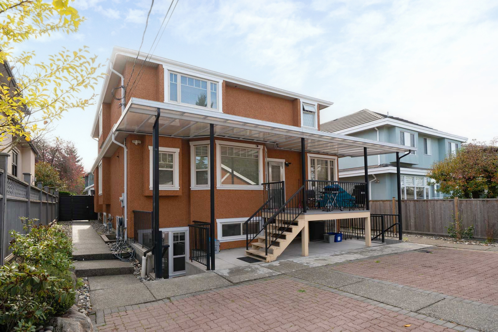 Two-story brown home on Yew St, Vancouver, featuring a covered back deck and brick-paved driveway.