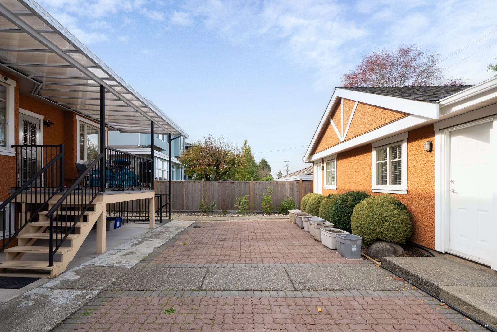 Patio on Yew St between two orange stucco buildings, featuring a raised deck with stairs and storage bins.