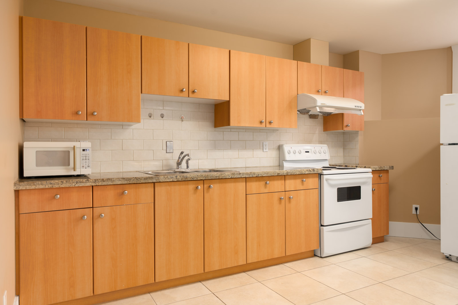 Kitchen in a West 22nd Ave Vancouver basement with light wood cabinets, granite countertops, and white appliances.