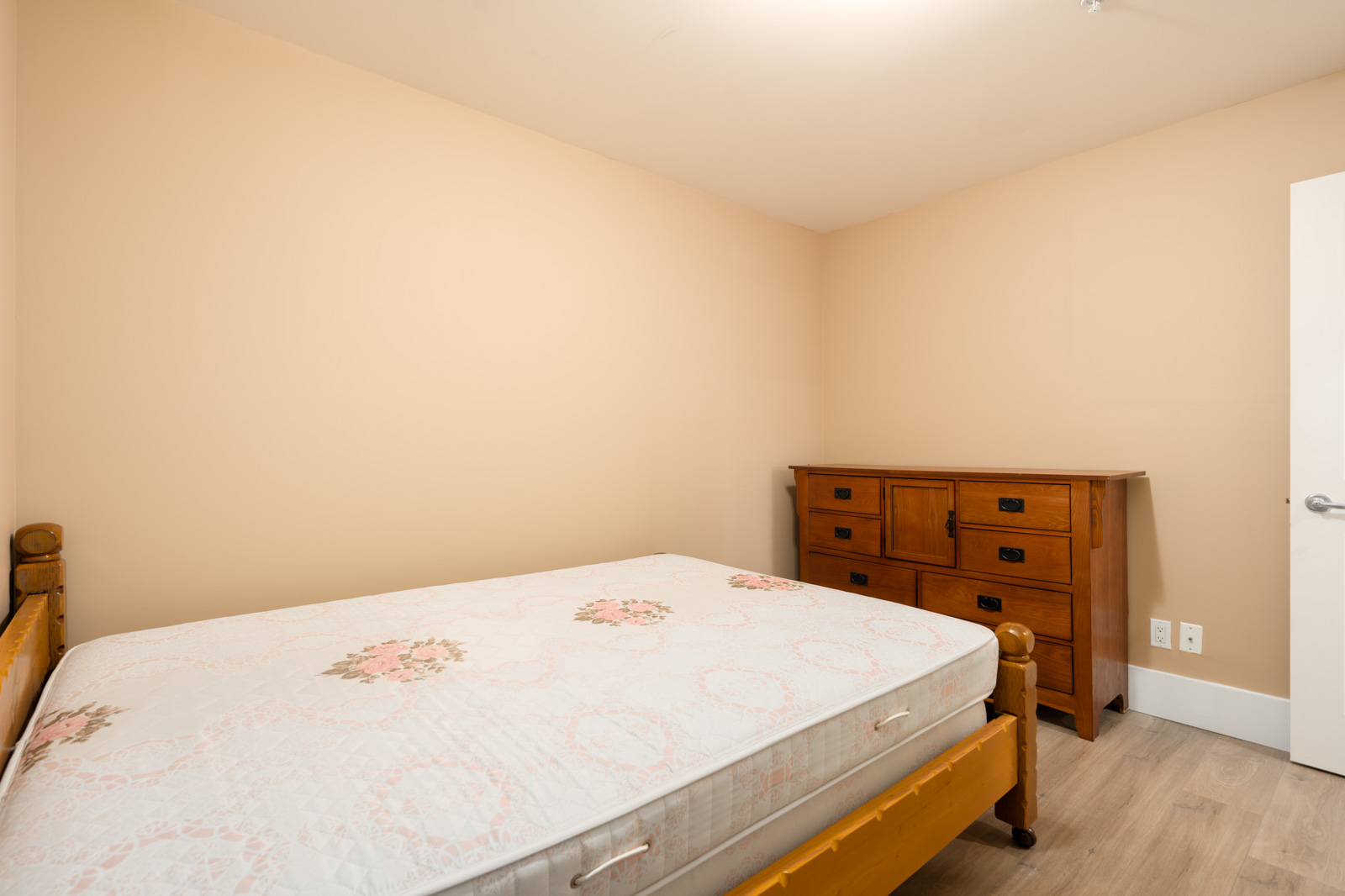 A wooden bed frame with a floral mattress and wooden dresser in a beige room on West 22nd Ave.